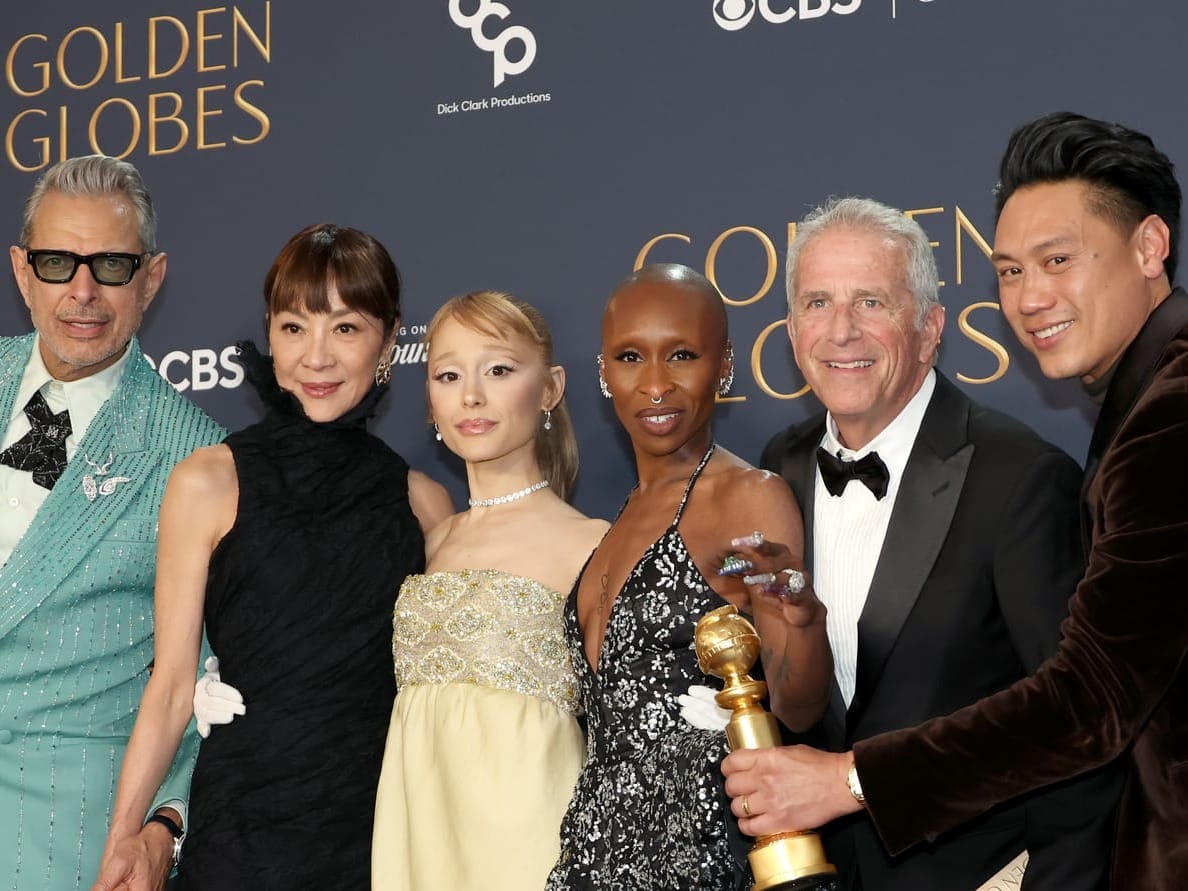 Jeff Goldblum, Michelle Yeoh, Ariana Grande, Cynthia Erivo, Marc Platt and Jon M. Chu holding the 2025 Cinematic and Box Office Achievement Golden Globe Award for “Wicked,”